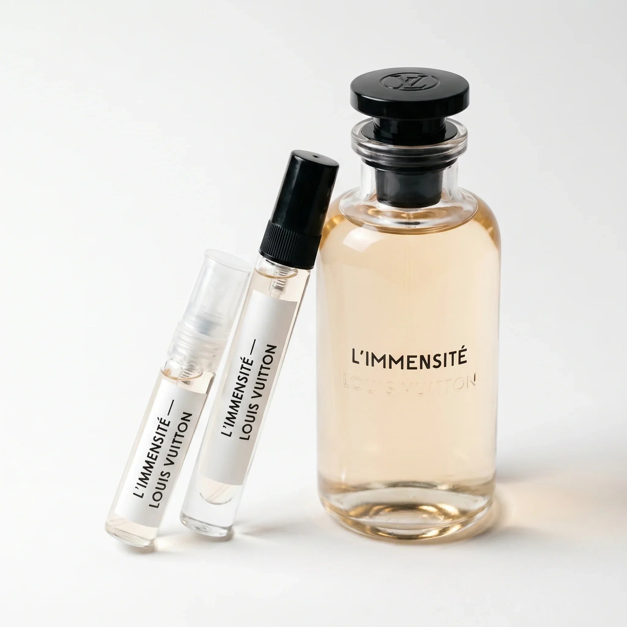 Louis Vuitton L'Immensité decant vials with clear glass apothecary bottle pale champagne honey amber juice black LV monogram cap on white background luxury fragrance photography