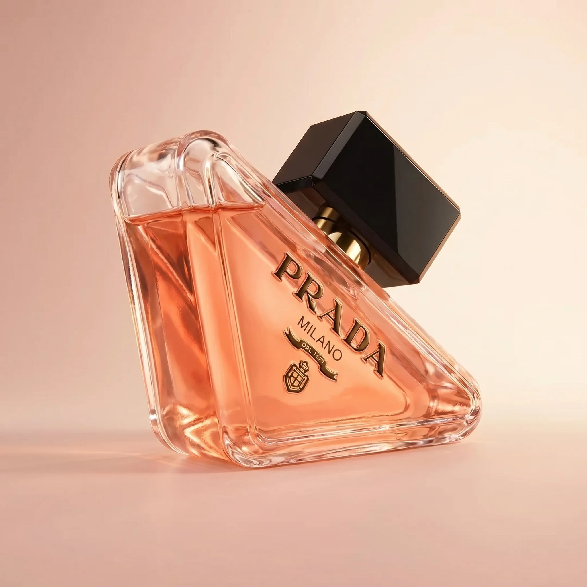 Prada Paradoxe EDP bottle at three-quarter angle showing faceted triangular glass and black-and-gold cap on a soft blush gradient