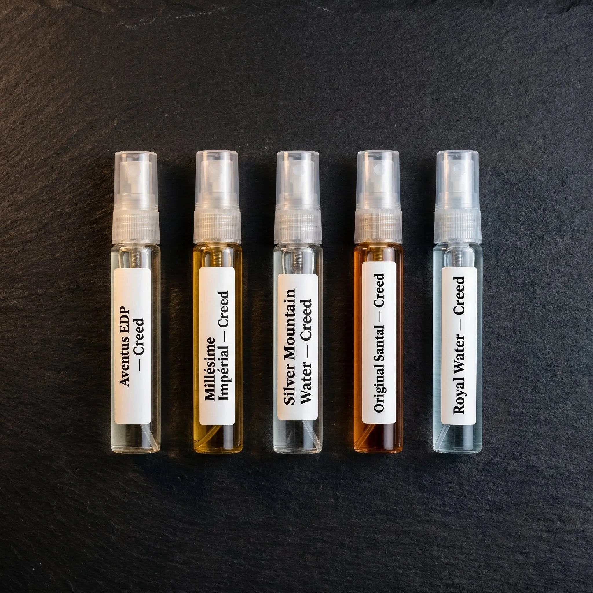 Top-down view of five Creed decants from the Aromatick Discovery Set on dark slate — Aventus EDP, Millésime Impérial, Silver Mountain Water, Original Santal, Royal Water