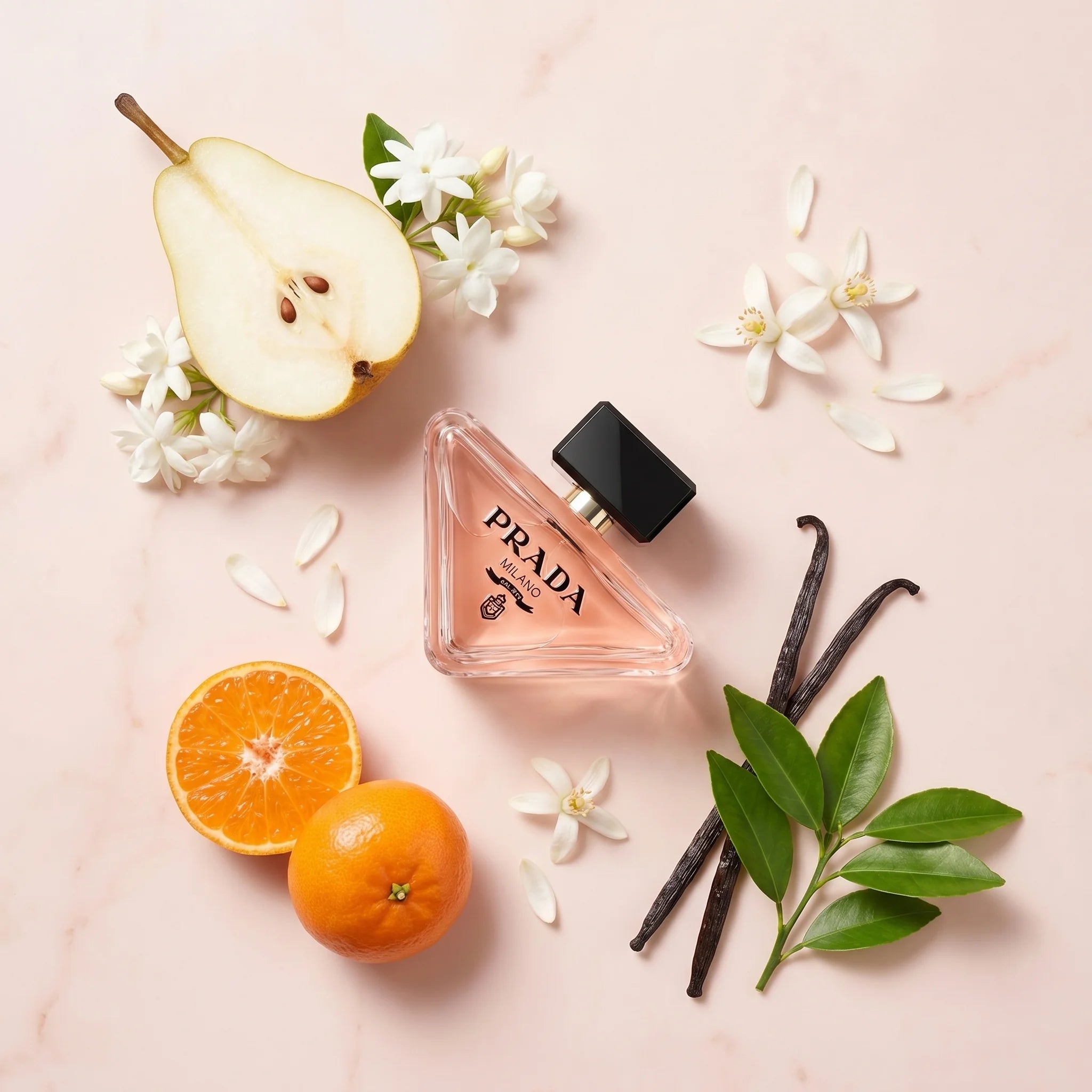 Prada Paradoxe EDP flatlay with halved pear, jasmine sambac, orange blossom, tangerine, vanilla pods and neroli leaves on blush marble