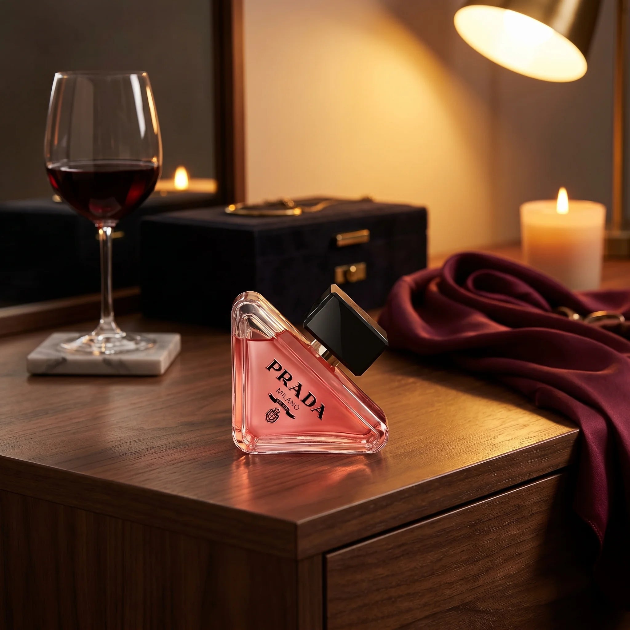 Prada Paradoxe Intense on a dark walnut vanity with red wine, velvet jewelry box and silk burgundy scarf in evening lamp light