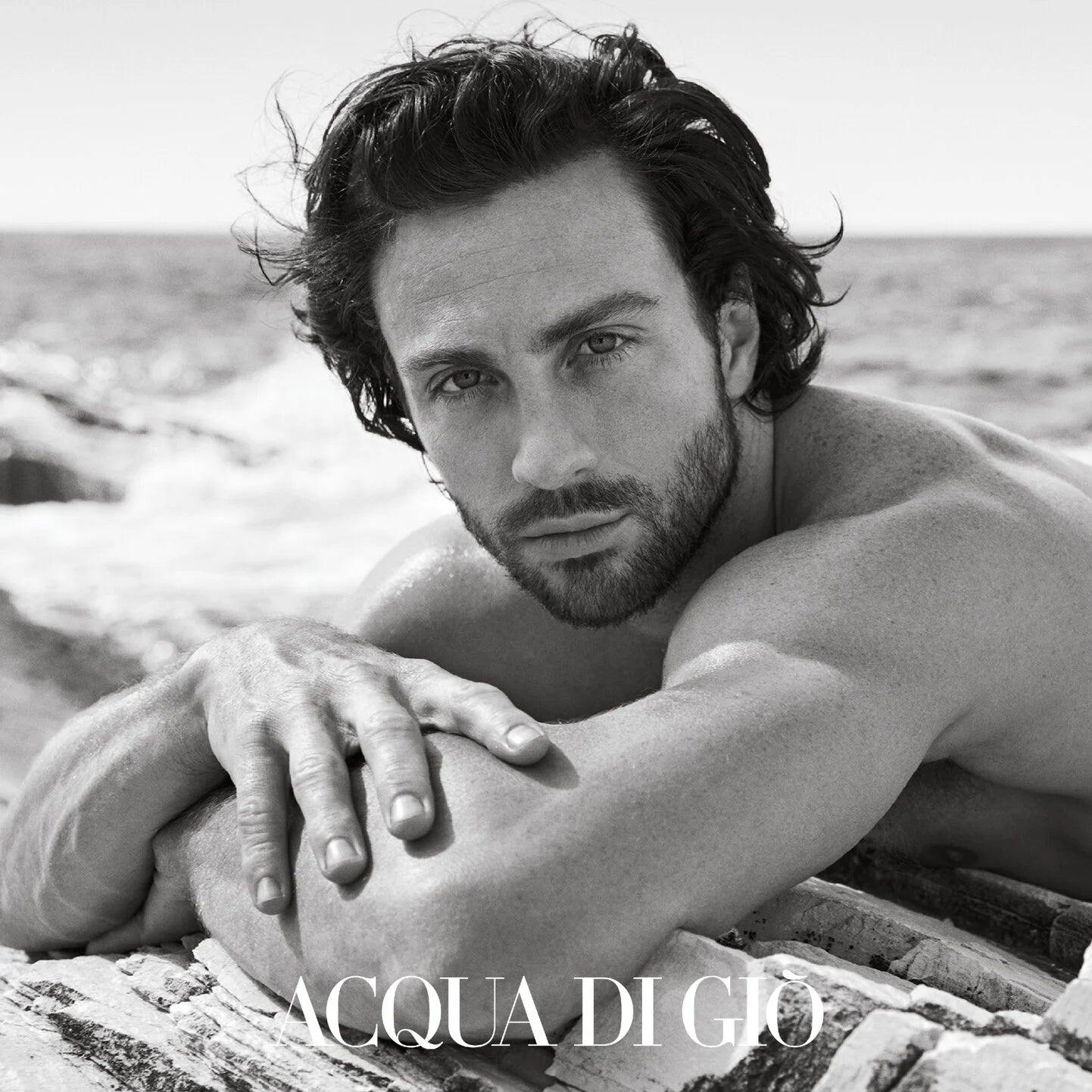 Man lying on a log by the water with 'Acqua di Gio' branding.