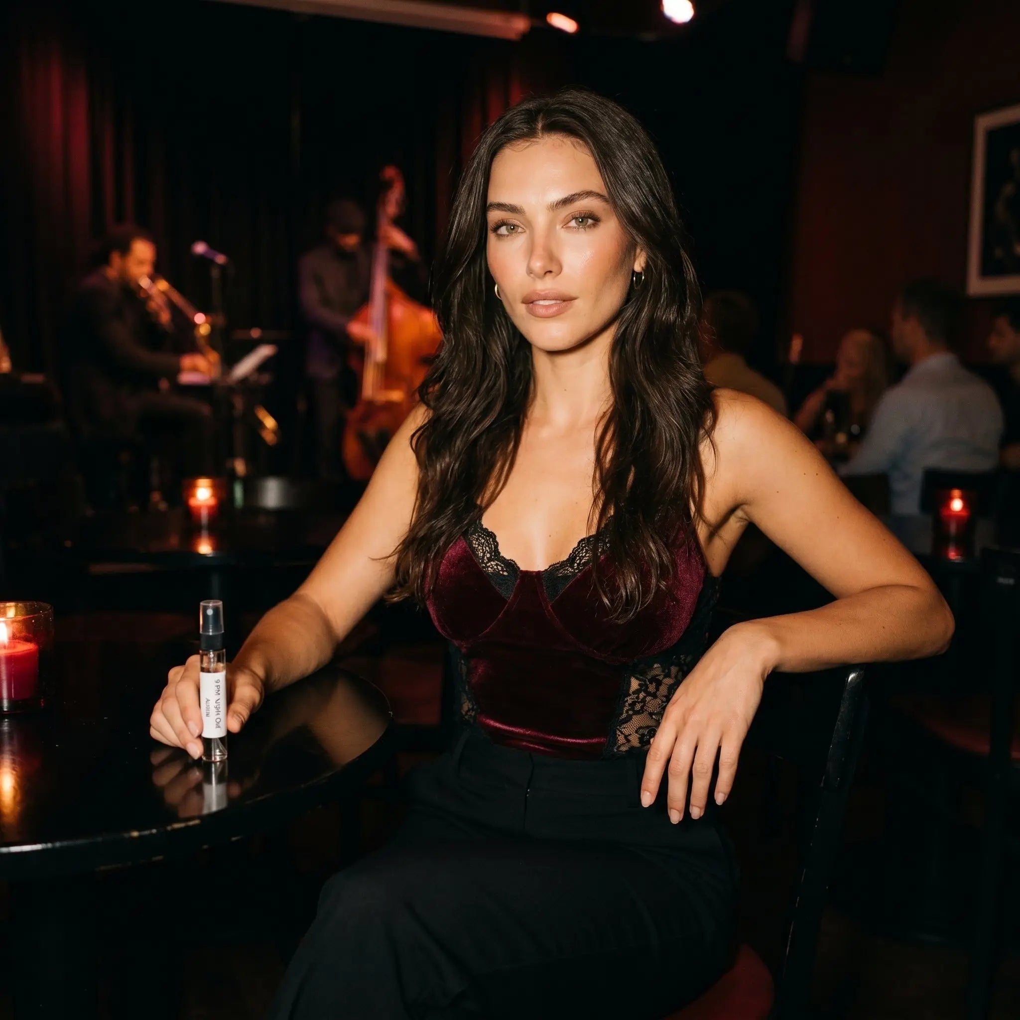 Woman in velvet top holding Afnan 9PM Night Out decant at candlelit jazz bar