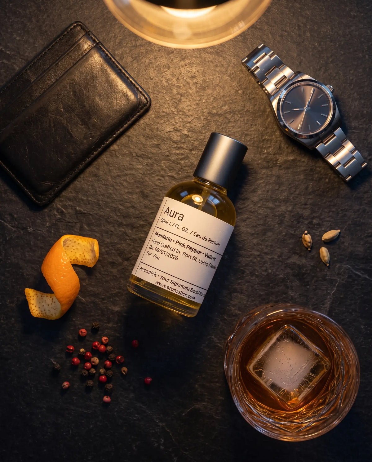 Aromatick Aura citrus spice men's fragrance on slate with orange peel, pink peppercorns, cardamom and a watch.