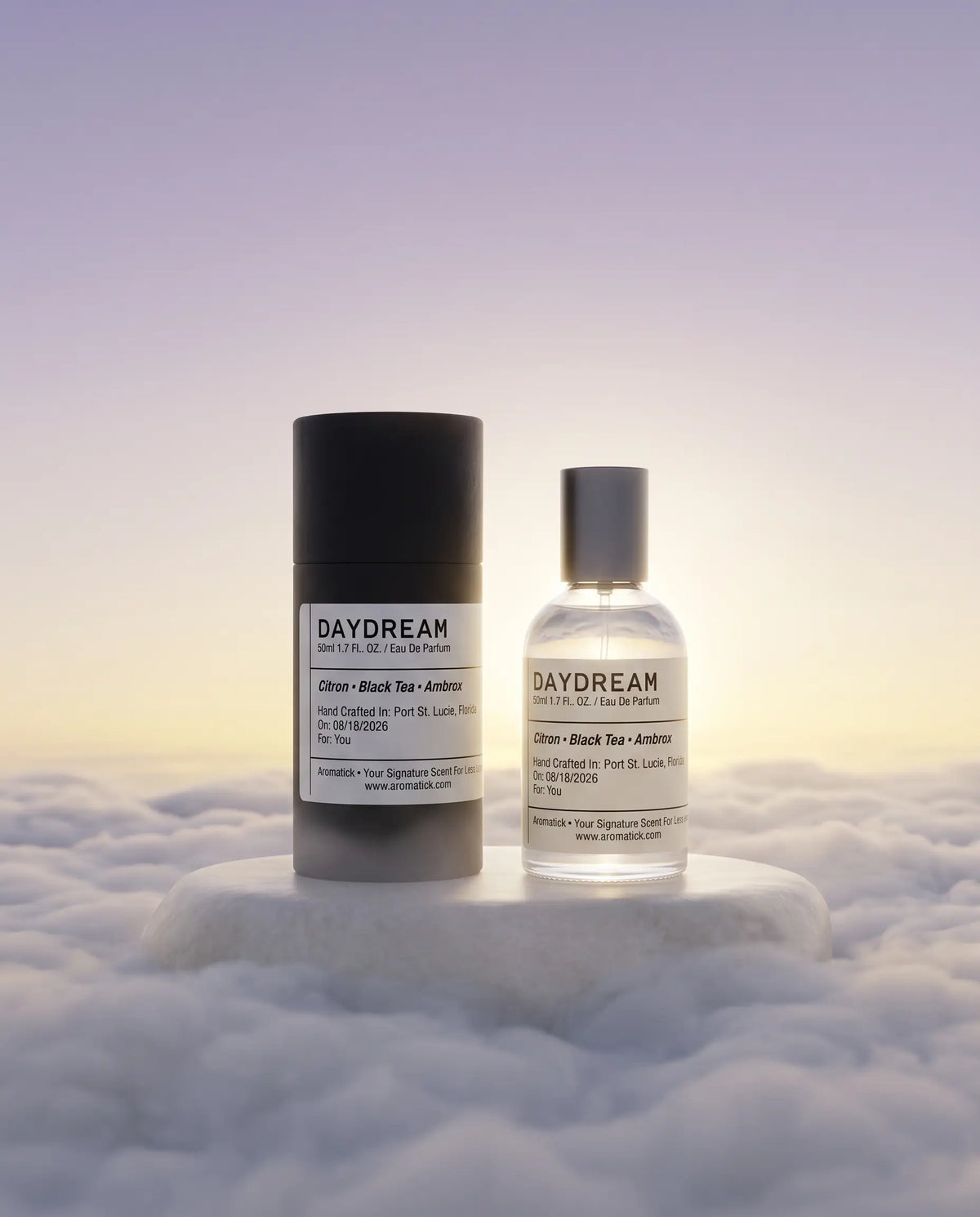 Aromatick Daydream 50ml eau de parfum bottle and black gift tube on a stone pedestal above sunrise clouds.