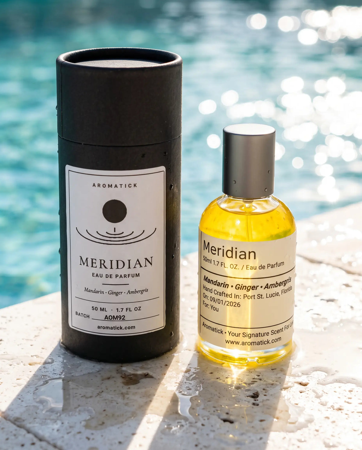Aromatick Meridian 50ml eau de parfum bottle beside its black gift tube on a sunlit poolside ledge.