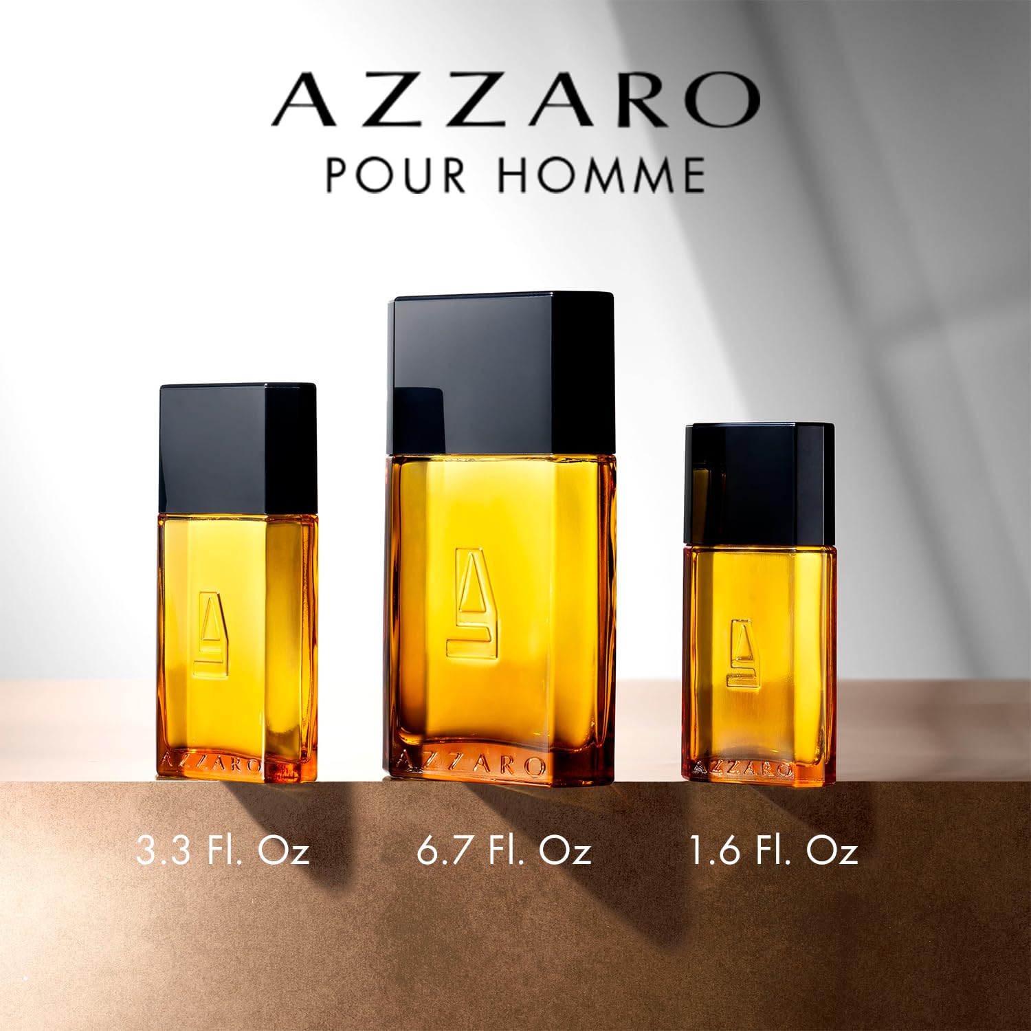 Three Azzaro Pour Homme perfume bottles of different sizes on a neutral background.