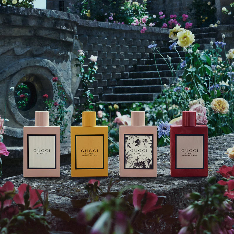 Four Gucci Bloom perfume bottles on a stone surface with a garden background