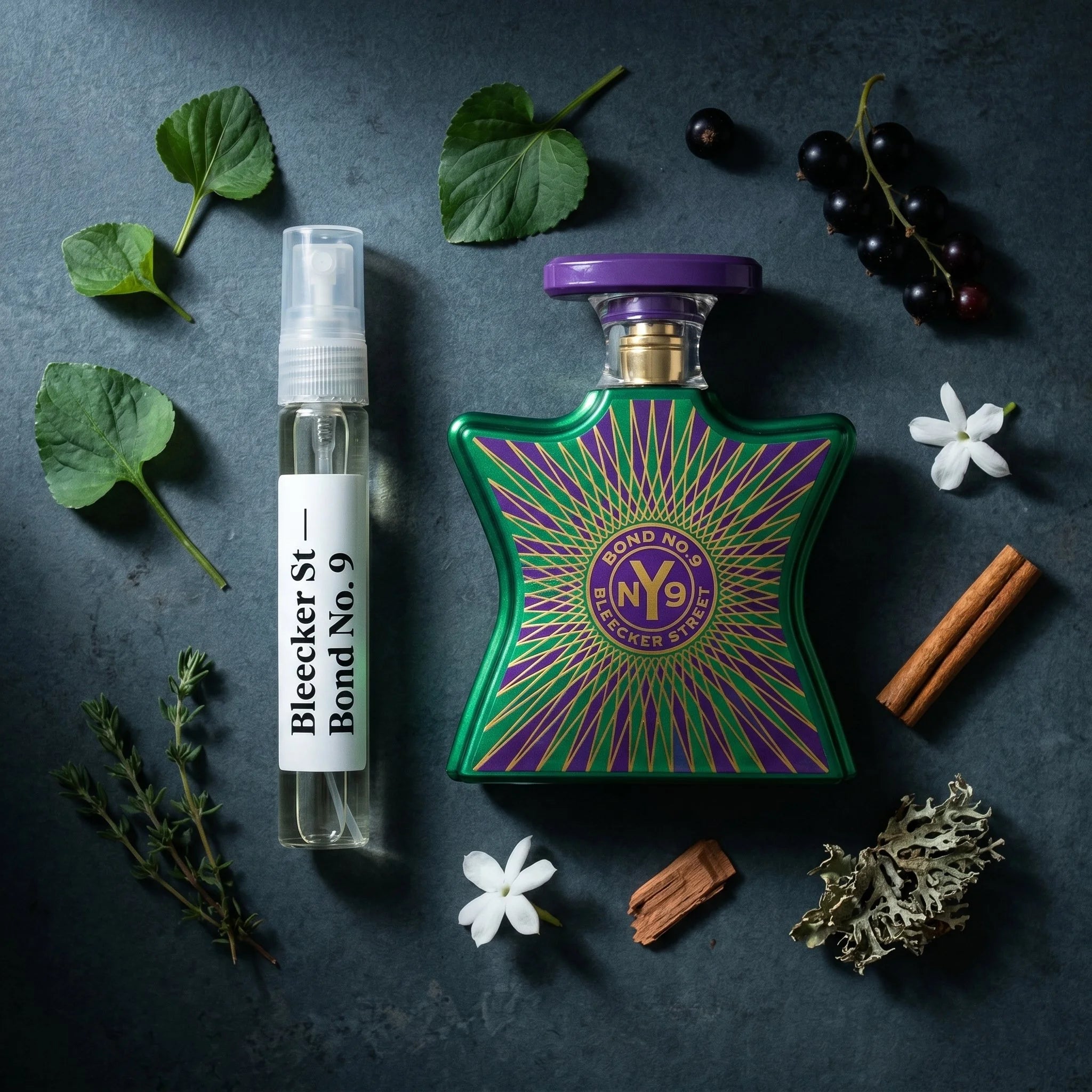 Bond No 9 Bleecker Street bottle and decant on dark urban concrete with violet leaf cassis thyme jasmine oakmoss vanilla fragrance notes flatlay