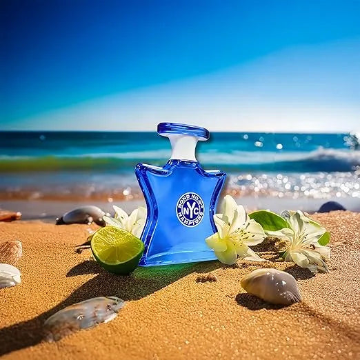 Blue perfume bottle with 'Bath & Body Works' logo on a sandy beach with flowers and a lime.