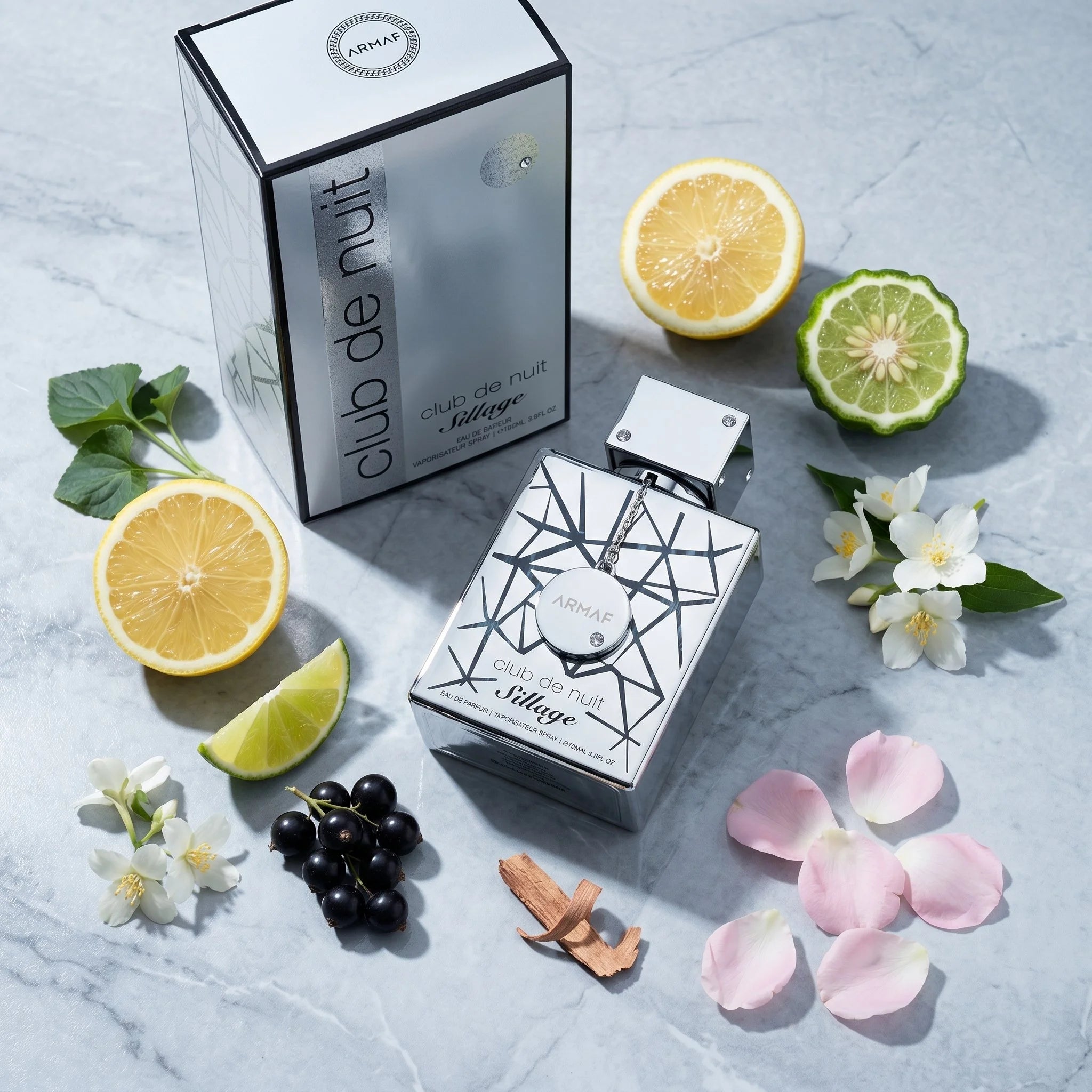 Armaf Club de Nuit Sillage EDP flatlay with lemon, lime, jasmine, black currant and cedarwood props