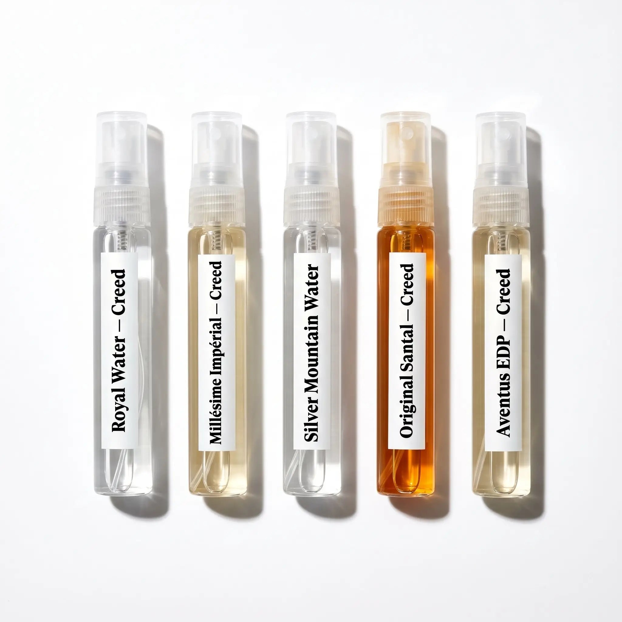 Creed discovery set decants flatlay — Royal Water, Millésime Impérial, Silver Mountain Water, Original Santal, Aventus EDP 5ml atomizers