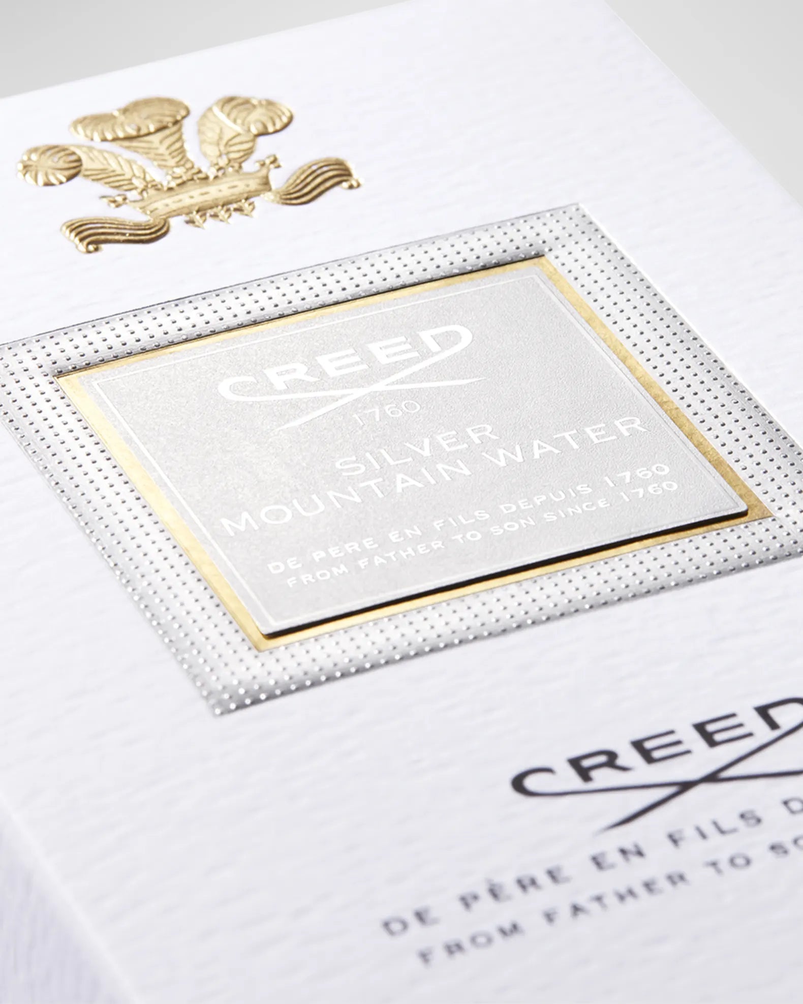 Close-up of Creed perfume packaging with gold emblem and text.