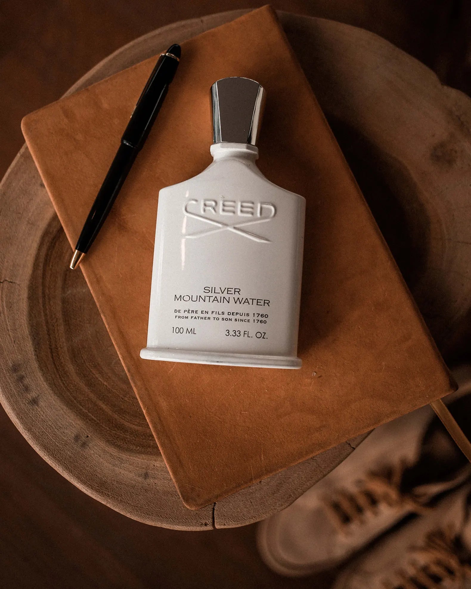 Creed Silver Mountain Water perfume bottle on a wooden surface with a notebook and pen.