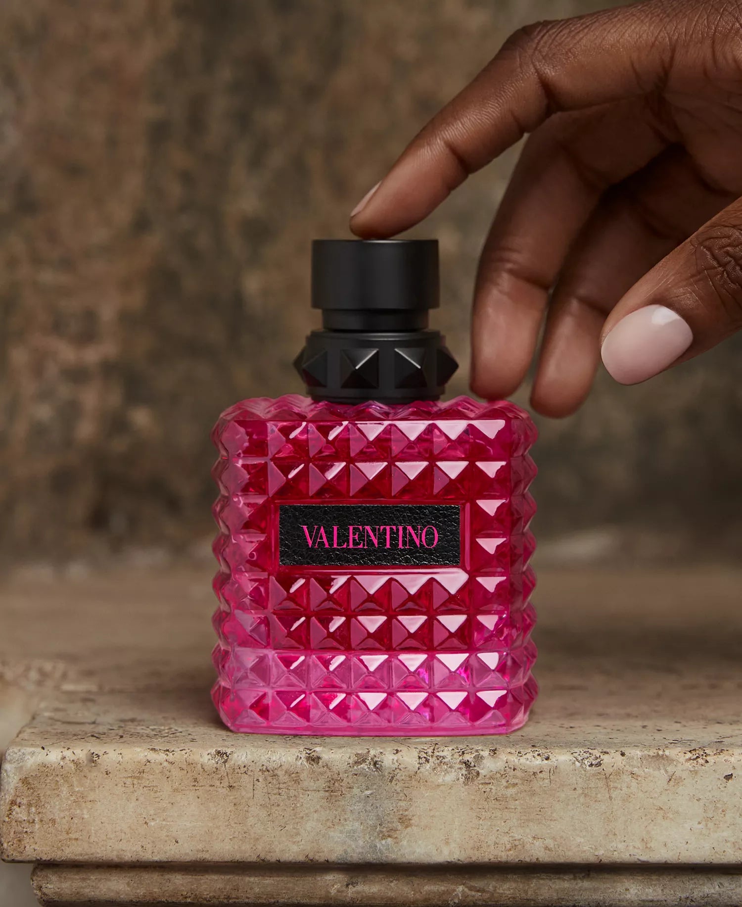 Pink perfume bottle with black cap held by a hand on a rustic surface