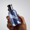 Hand holding a blue bottle labeled 'Gucci' against a blurred background