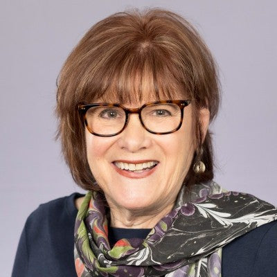 Woman wearing glasses and a patterned scarf against a plain background