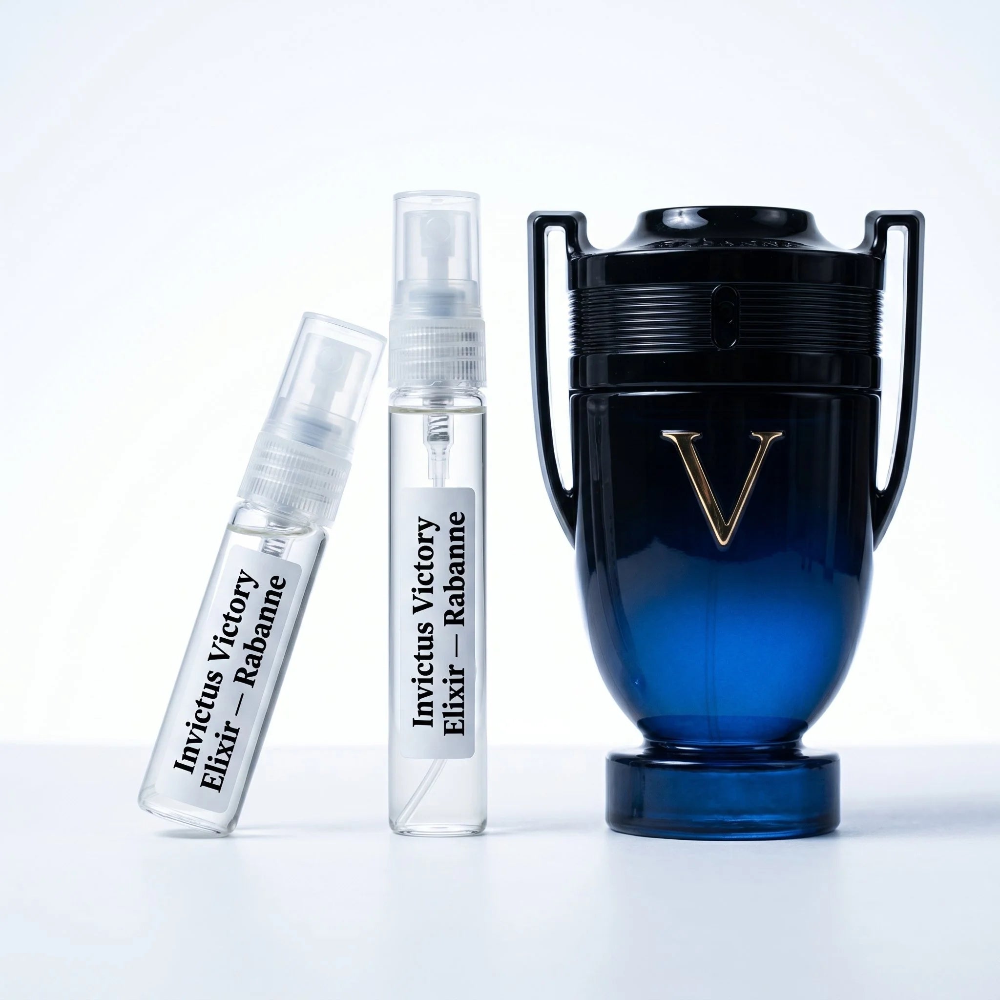 Rabanne Invictus Victory Elixir decant vials with navy blue black trophy bottle gold V on white background luxury fragrance photography