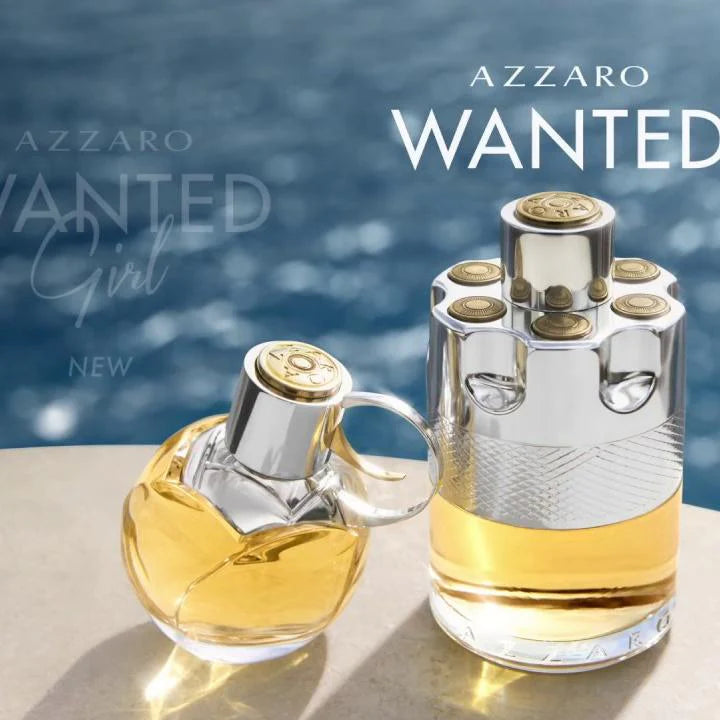 Two Azzaro Wanted perfume bottles on a reflective surface with water in the background