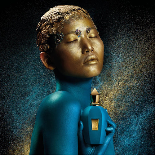 Blue-skinned figure holding a perfume bottle with a gold cap against a dark background