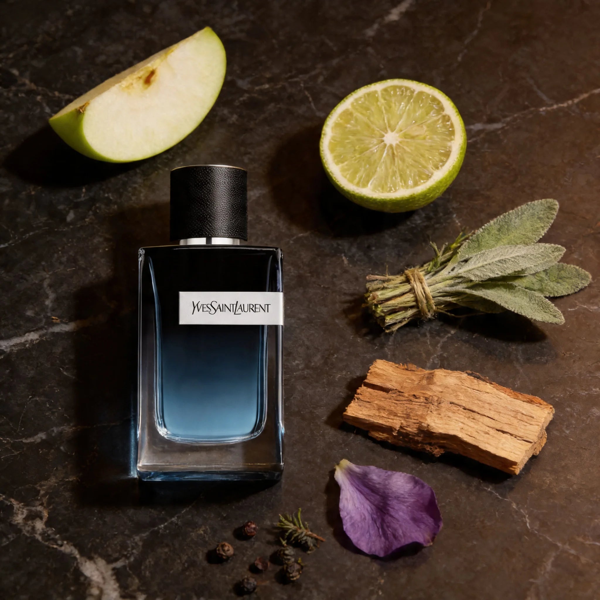 YSL perfume bottle with a half-apple, lime, and herbs on a dark surface