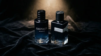 Two luxury cologne bottles paired on black velvet — YSL Y EDP and Dior Sauvage EDP as a seasonal fragrance rotation available at Aromatick at 30 to 60 percent below retail