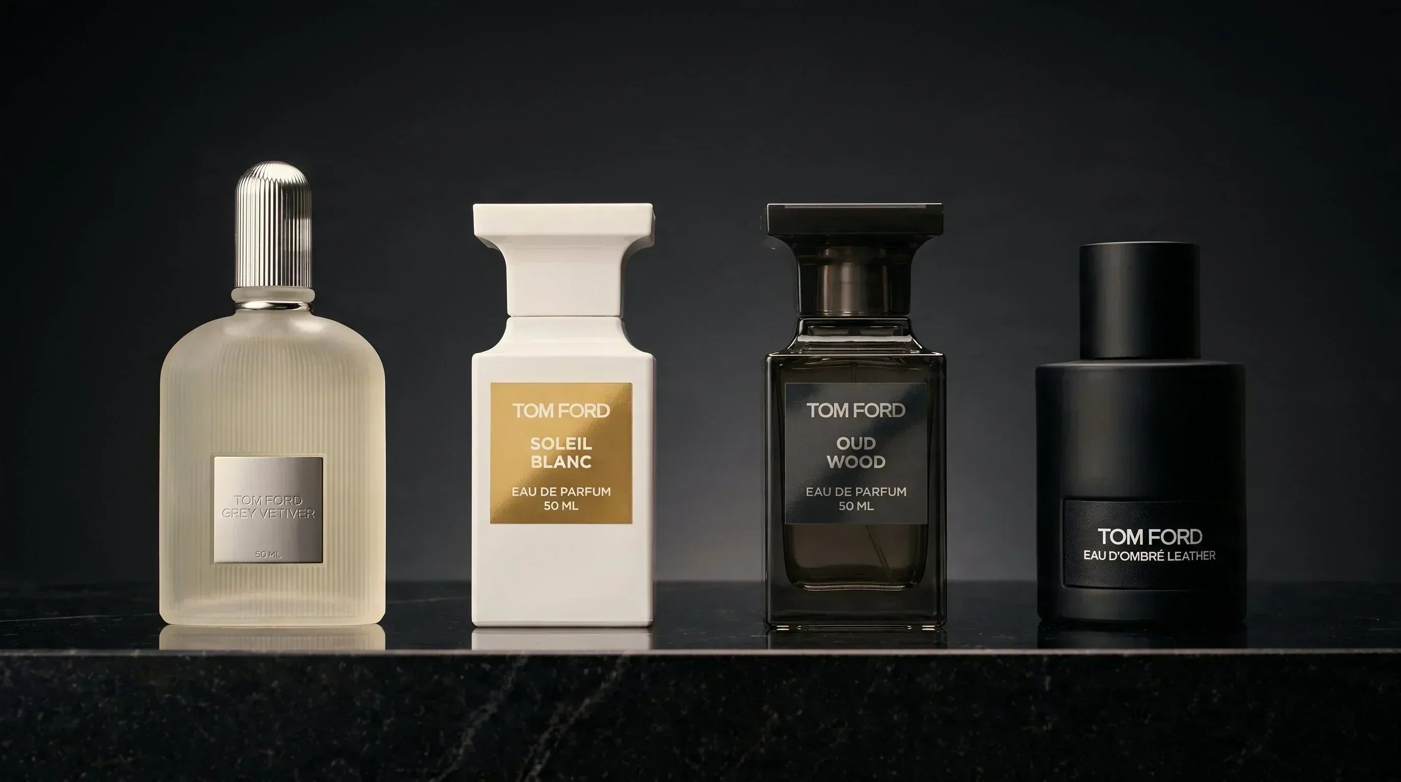Tom Ford fragrance lineup — Grey Vetiver, Soleil Blanc, Oud Wood, Eau d'Ombré Leather on black granite