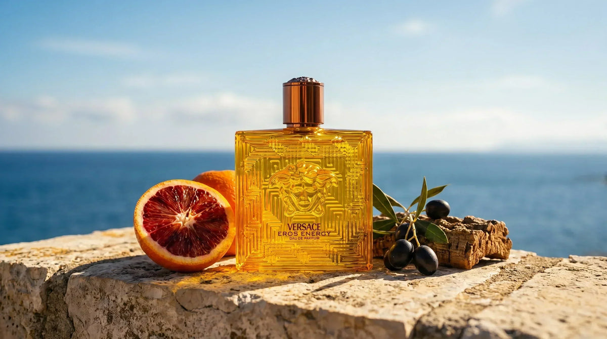 Versace Eros Energy EDP amber gold bottle on Mediterranean limestone wall with blood orange and sea backdrop