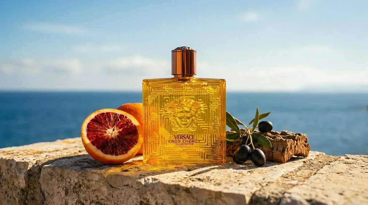 Versace Eros Energy EDP amber gold bottle on Mediterranean limestone wall with blood orange and sea backdrop