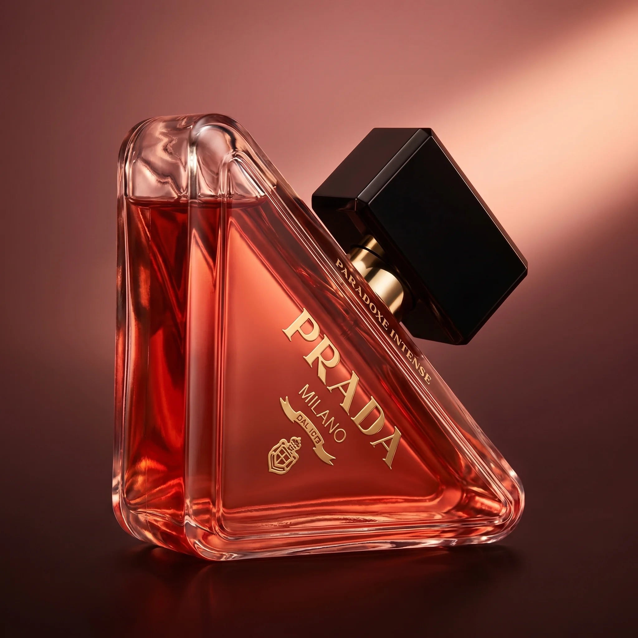 Prada Paradoxe Intense bottle at three-quarter angle on a rose-burgundy gradient with evening-mood directional lighting
