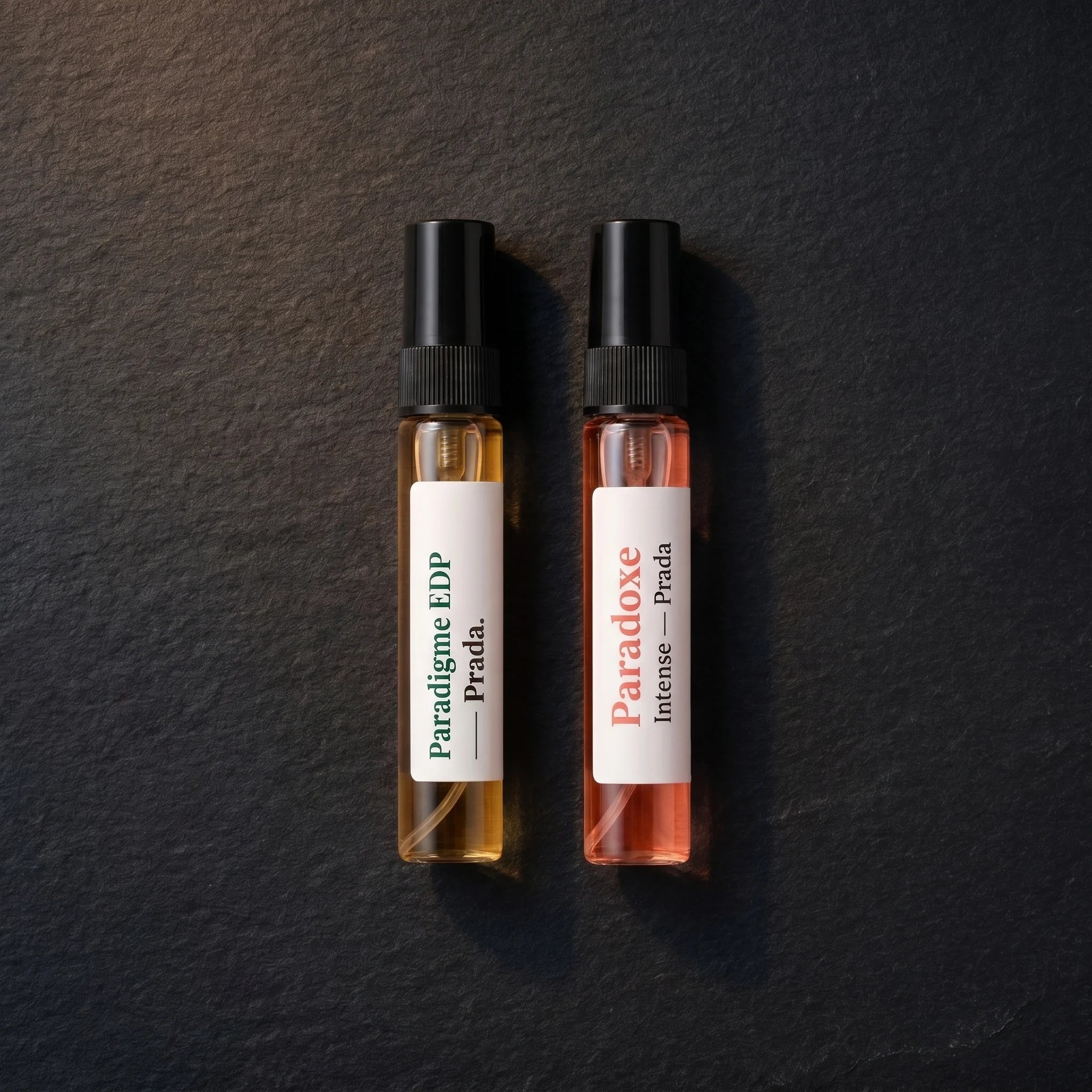 Top-down view of two Prada decants from the Aromatick His & Hers Discovery Set on dark slate — Paradigme EDP for him and Paradoxe Intense EDP for her