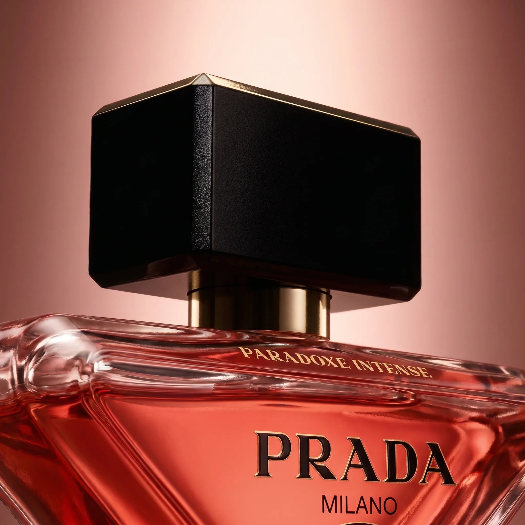 Macro detail of Prada Paradoxe Intense cap and shoulders — black magnetic top with gold accent over coral-red juice
