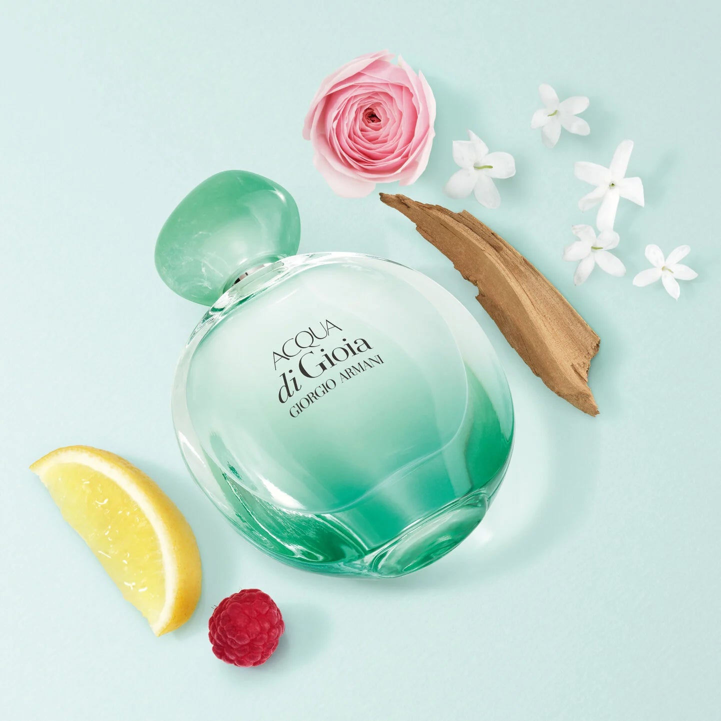 Green perfume bottle labeled 'Acqua di Gioia' by Giorgio Armani with flowers and a lemon wedge on a light blue background.