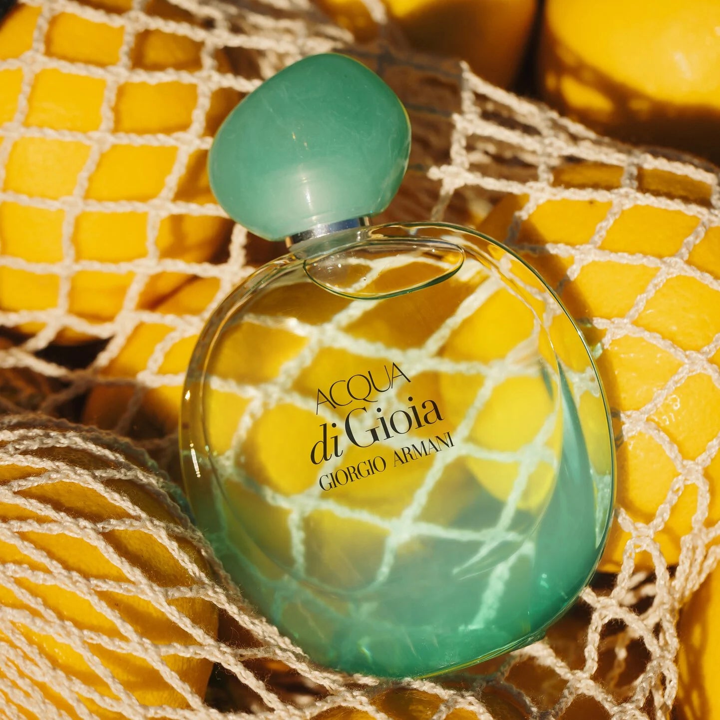 Perfume bottle of Acqua di Gioia by Giorgio Armani on a textured surface with lemons.