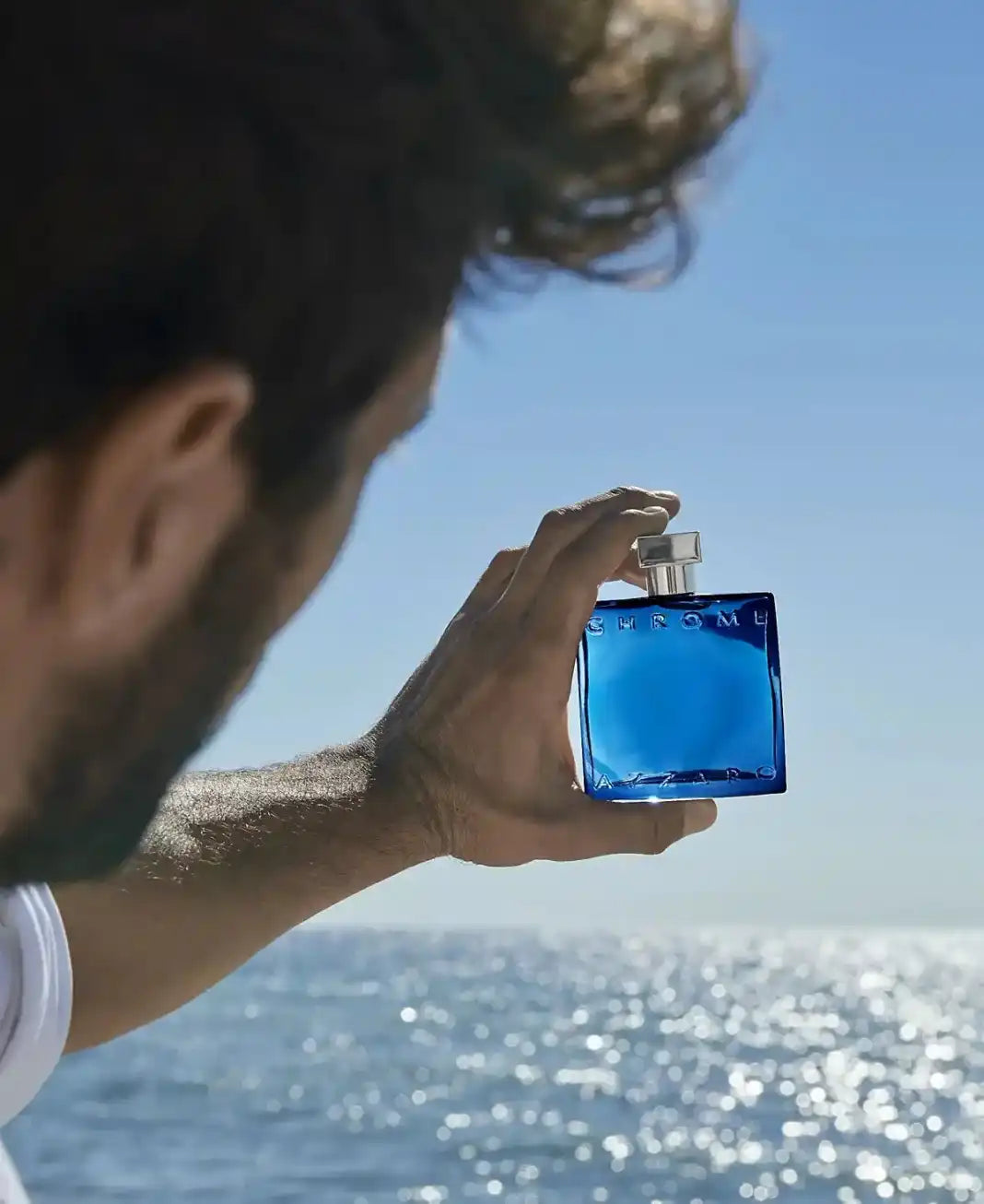 Person holding a blue perfume bottle by the ocean