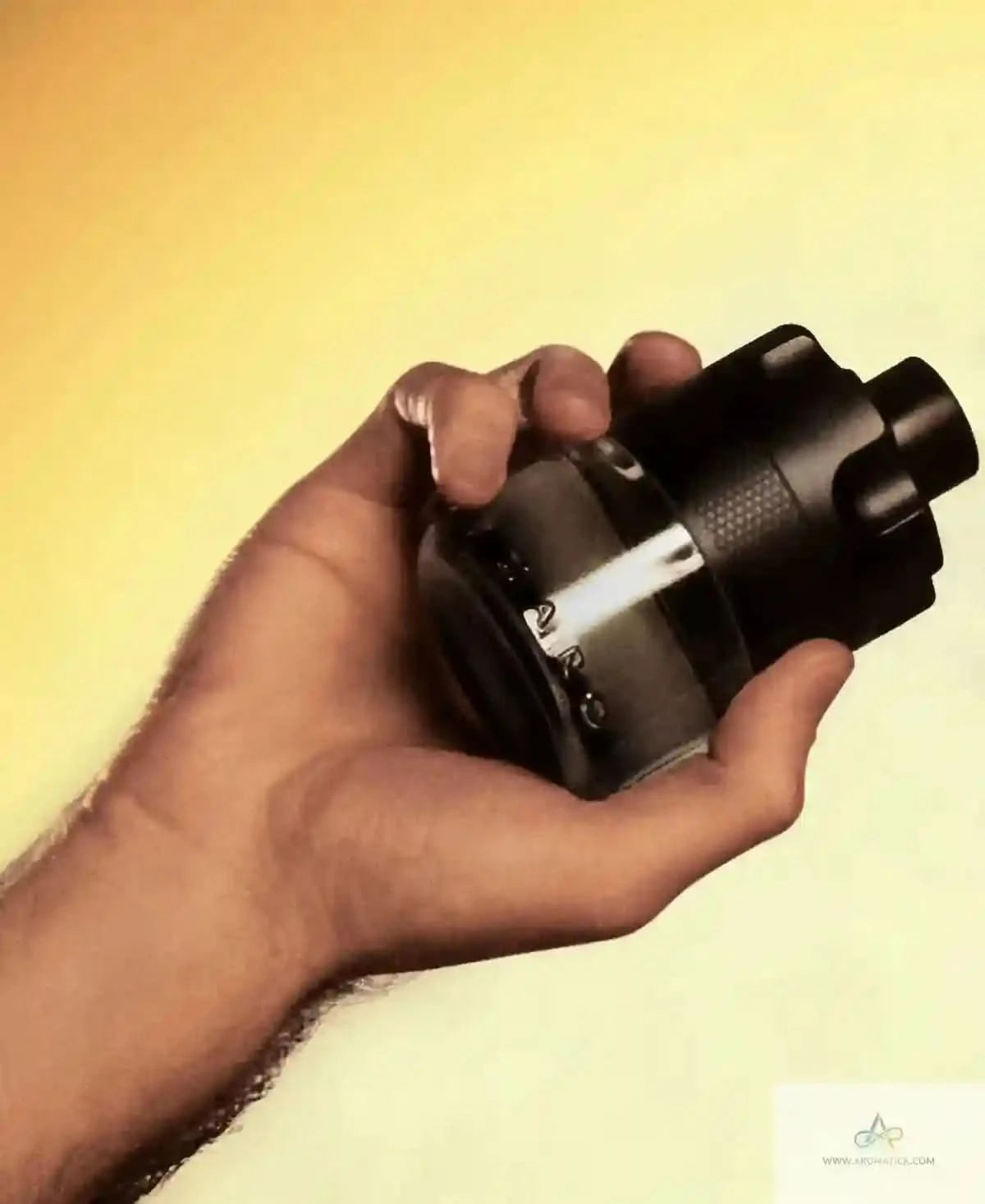 Hand holding a black spray bottle against a yellow background