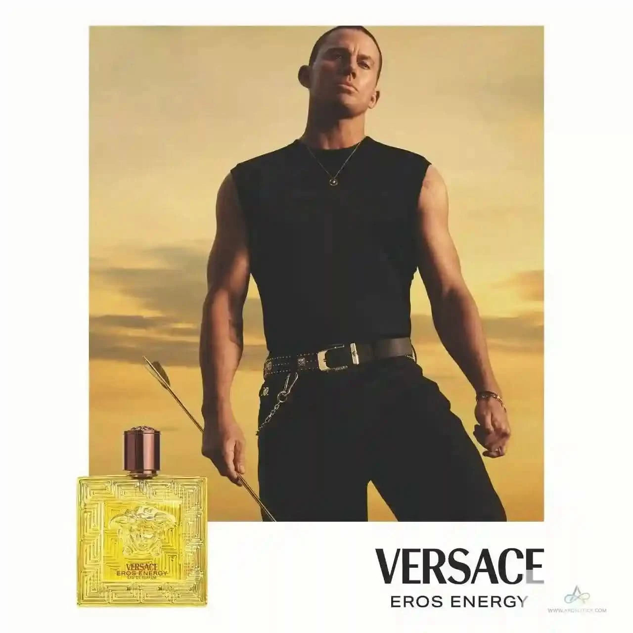 Man holding a spear with a Versace Eros Energy perfume bottle in front of him against a yellow sky.