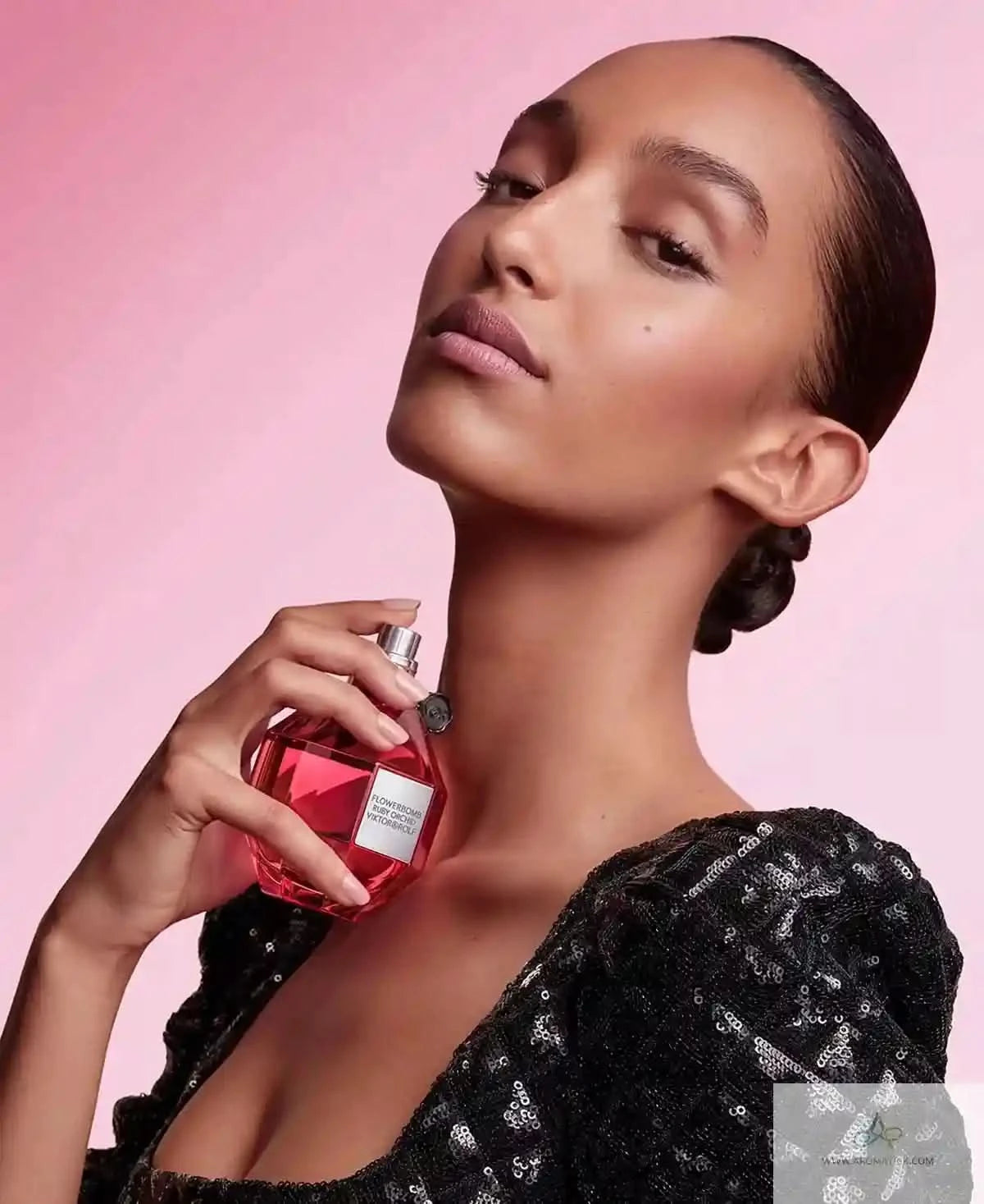 Woman holding a red perfume bottle against a pink background