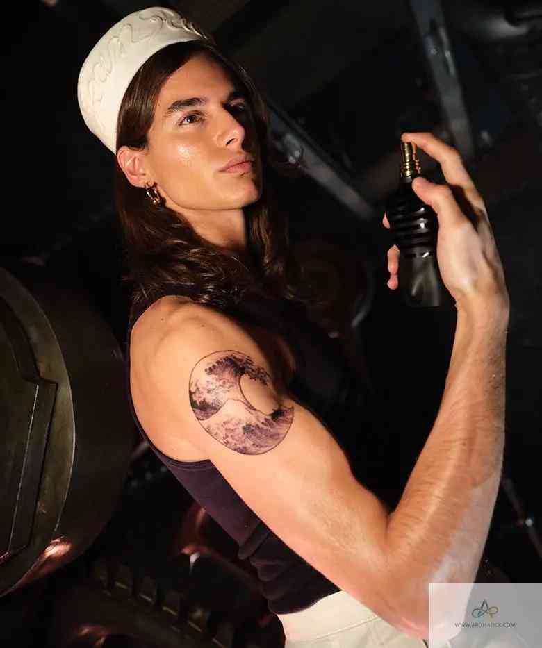 Model applying Le Male Le Parfum - Aromatick men's fragrance, showcasing the bold black bottle in a stylish grooming setting.