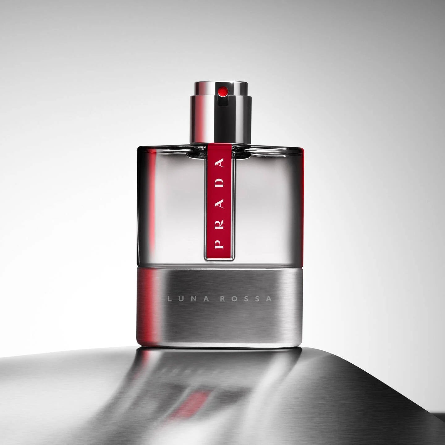Prada Luna Rossa perfume bottle on a reflective surface with a gray background