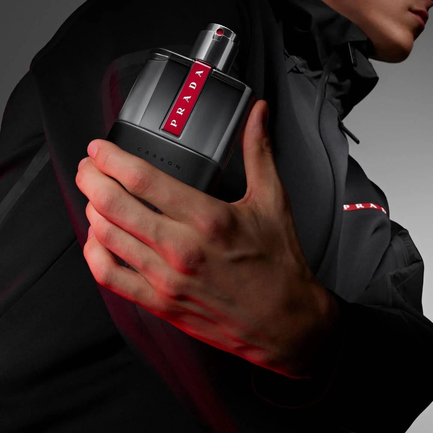 Person holding a Prada fragrances bottle with a dark background