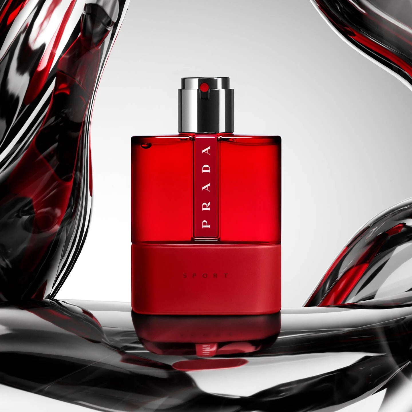 Red Prada perfume bottle on a reflective surface with abstract shapes in the background