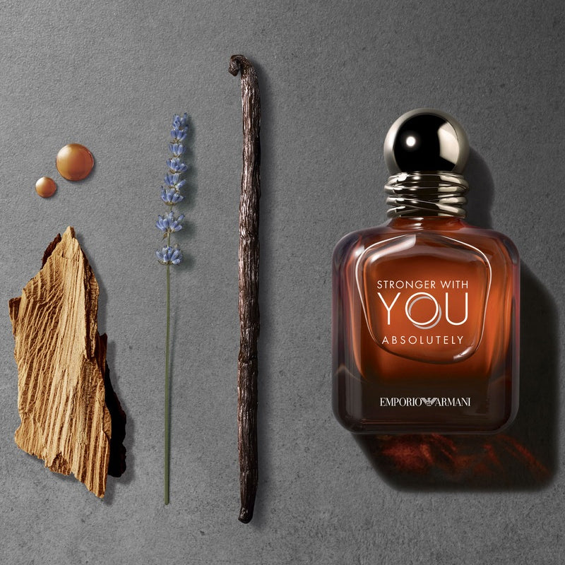 Perfume bottle labeled 'Stronger with You Absolutely' by Emporio Armani on a gray background with vanilla bean, lavender, and wood.