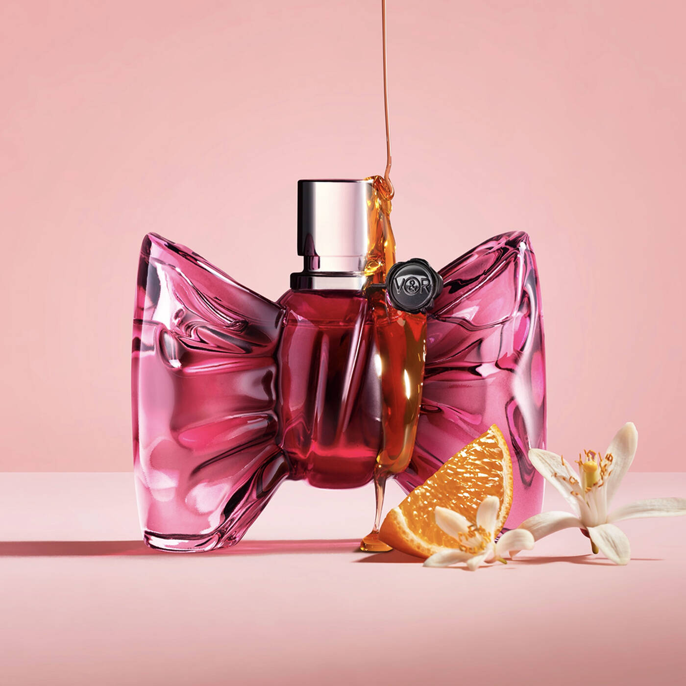 Pink bow-shaped perfume bottle with orange slice and flowers on a pink background