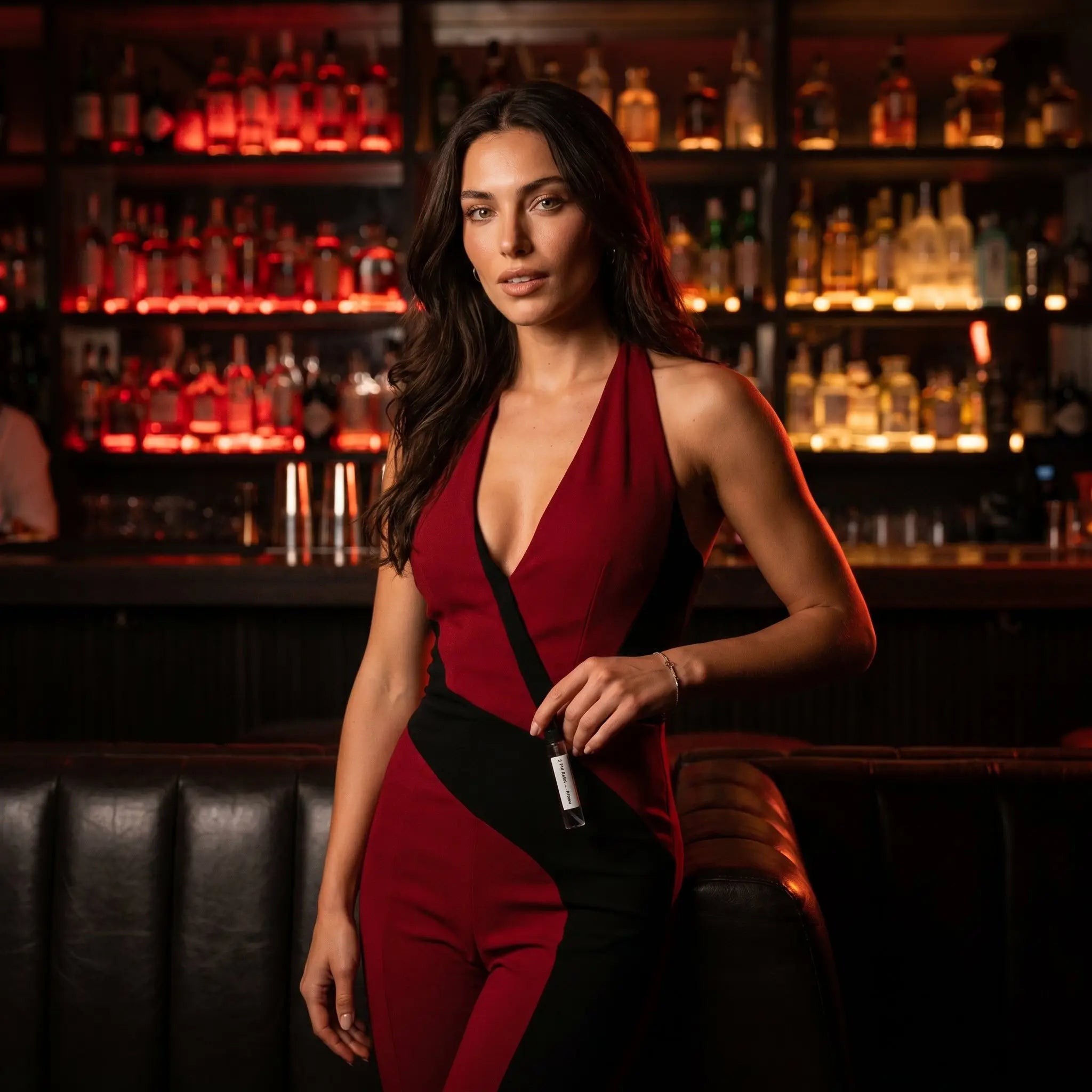 Woman in red dress holding Afnan 9PM Rebel decant at upscale cocktail bar

