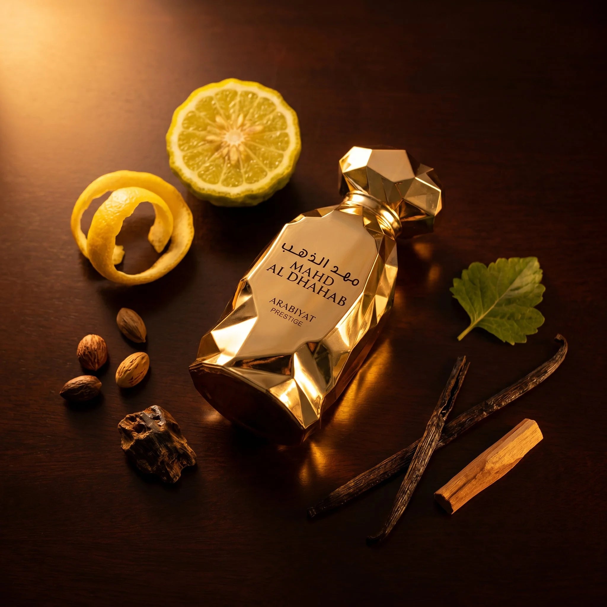 Arabiyat Prestige Mahd Al Dhahab EDP flatlay with bergamot, lemon, vanilla bean, oud, sandalwood on dark wood surface
