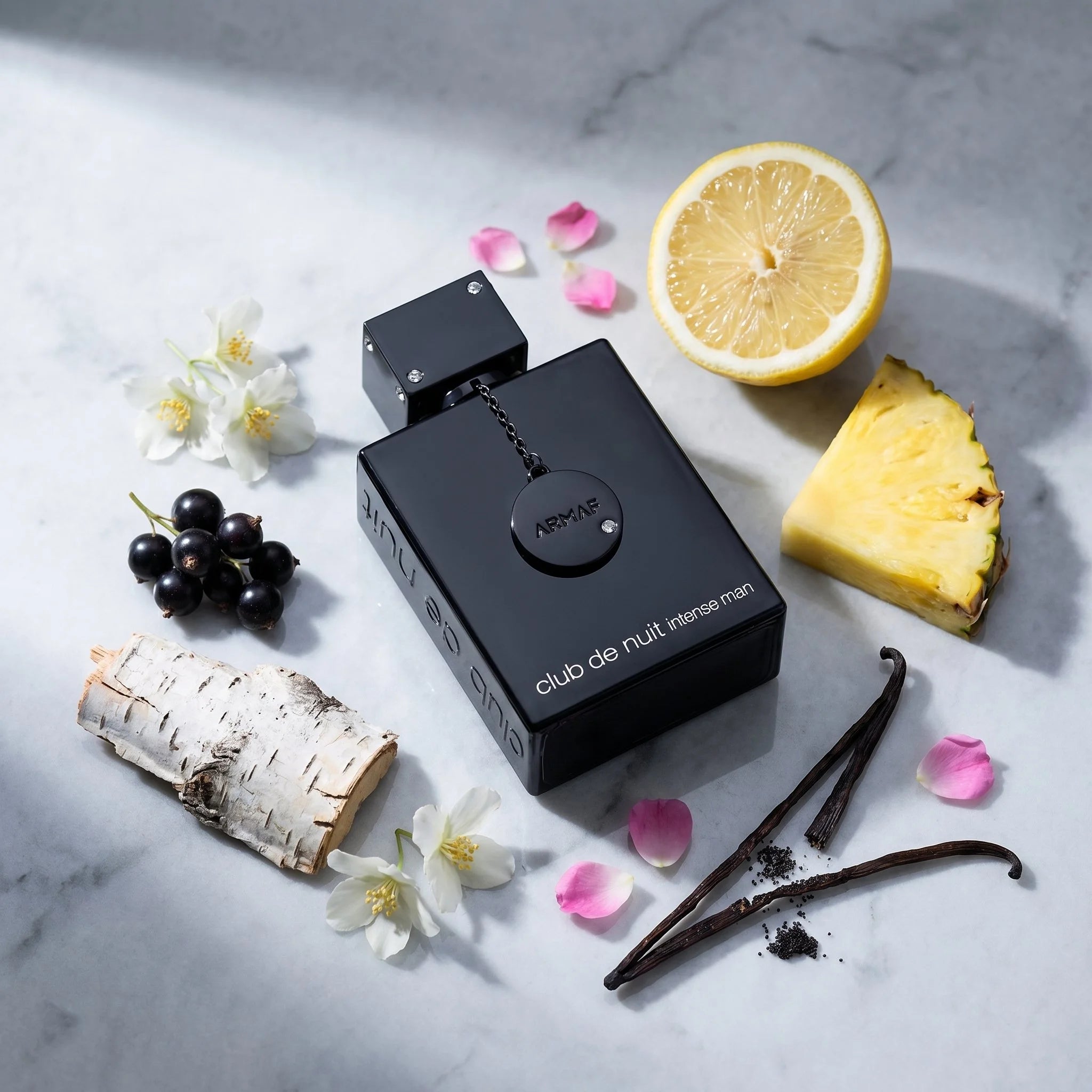 Armaf Club de Nuit Intense Man EDT flatlay with lemon, pineapple, black currant, jasmine, birch, vanilla bean on marble
