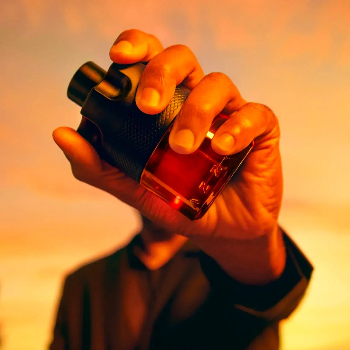 Hand holding a perfume bottle with a warm, blurred background