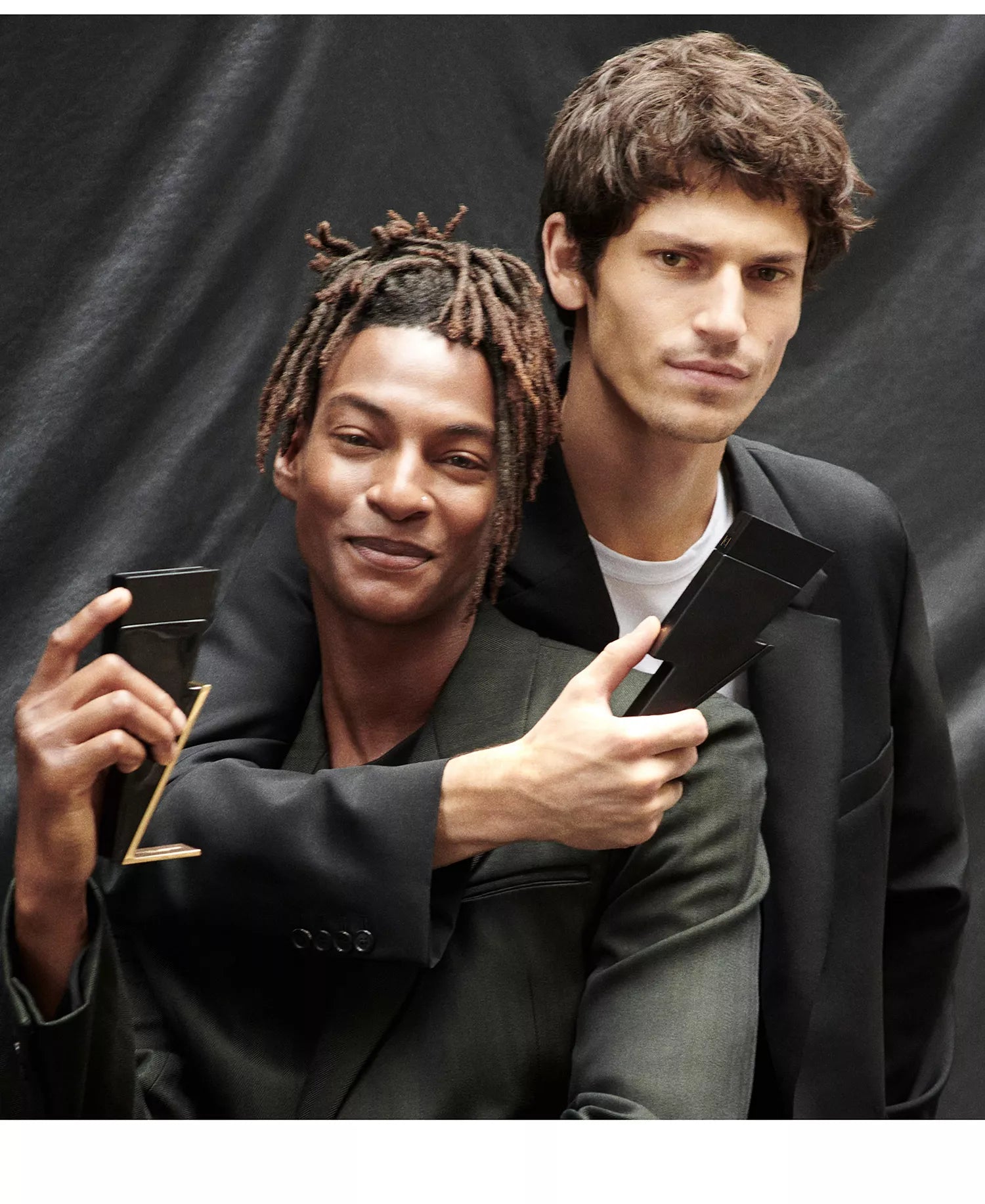 Two men holding black suit jackets against a black background