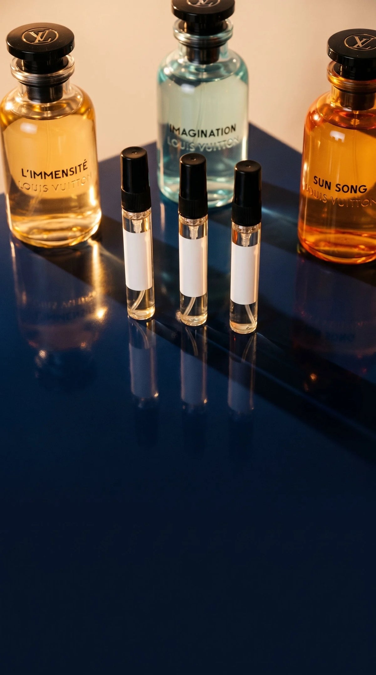 Three Louis Vuitton decant vials in front of L'Immensite, Imagination, and Sun Song bottles on navy surface
